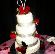 A lovely wedding cake with fresh red roses around it.